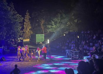 Μια δυναμική σκηνή χορευτών στο Υπαίθριο Θέατρο Σερβίων κατά τη διάρκεια του Φεστιβάλ Σερβίων, με το κοινό να παρακολουθεί με ενθουσιασμό.