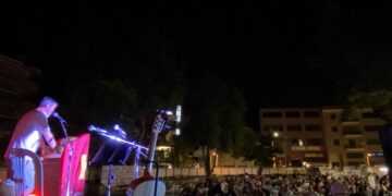 Μια σκηνή από το Φεστιβάλ ΚΝΕ – Οδηγητή, με έναν ομιλητή στο βήμα και πλήθος κόσμου να παρακολουθεί σε μια νυχτερινή πλατεία.