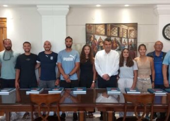 Μέλη της εθνικής κωπηλασίας στέκονται όρθια σε ένα δωμάτιο στην Καστοριά, έτοιμοι για το Παγκόσμιο Πρωτάθλημα.