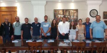 Μέλη της εθνικής κωπηλασίας στέκονται όρθια σε ένα δωμάτιο στην Καστοριά, έτοιμοι για το Παγκόσμιο Πρωτάθλημα.