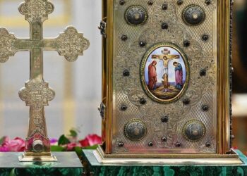 Ένας χρυσός σταυρός και ένα βιβλίο με αναπαράσταση του Χριστού στο σταυρό, τοποθετημένα σε μια πράσινη βάση με ροζ πέταλα, συμβολίζουν την Υψωση του Τιμίου Σταυρού στη Φλώρινα.