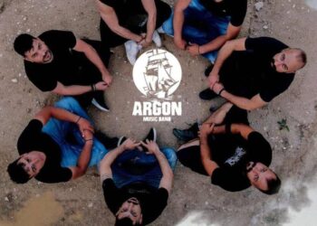 Μια ομάδα νεαρών ανδρών, μέλη του συγκροτήματος «ARGON», πόζαραν χαμογελαστοί στον αύλειο χώρο του Δημοτικού Σχολείου Μικροκάστρου για την επερχόμενη γιορτή καπνού.