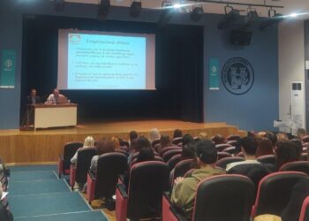 Ένας άνδρας μιλάει σε ένα κοινό στην εκδήλωση για τη Διπολική Διαταραχή στη Φλώρινα, με μια διαφάνεια να προβάλλεται στο παρασκήνιο.