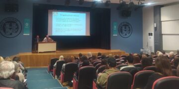 Ένας άνδρας μιλάει σε ένα κοινό στην εκδήλωση για τη Διπολική Διαταραχή στη Φλώρινα, με μια διαφάνεια να προβάλλεται στο παρασκήνιο.