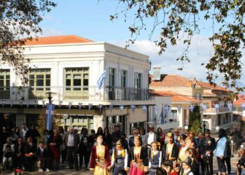 Σέρβια 28ης Οκτωβρίου: Χορευτές σε παραδοσιακές στολές χορεύουν στην Κεντρική Πλατεία των Σερβίων με θεατές και ελληνικές σημαίες στο φόντο.