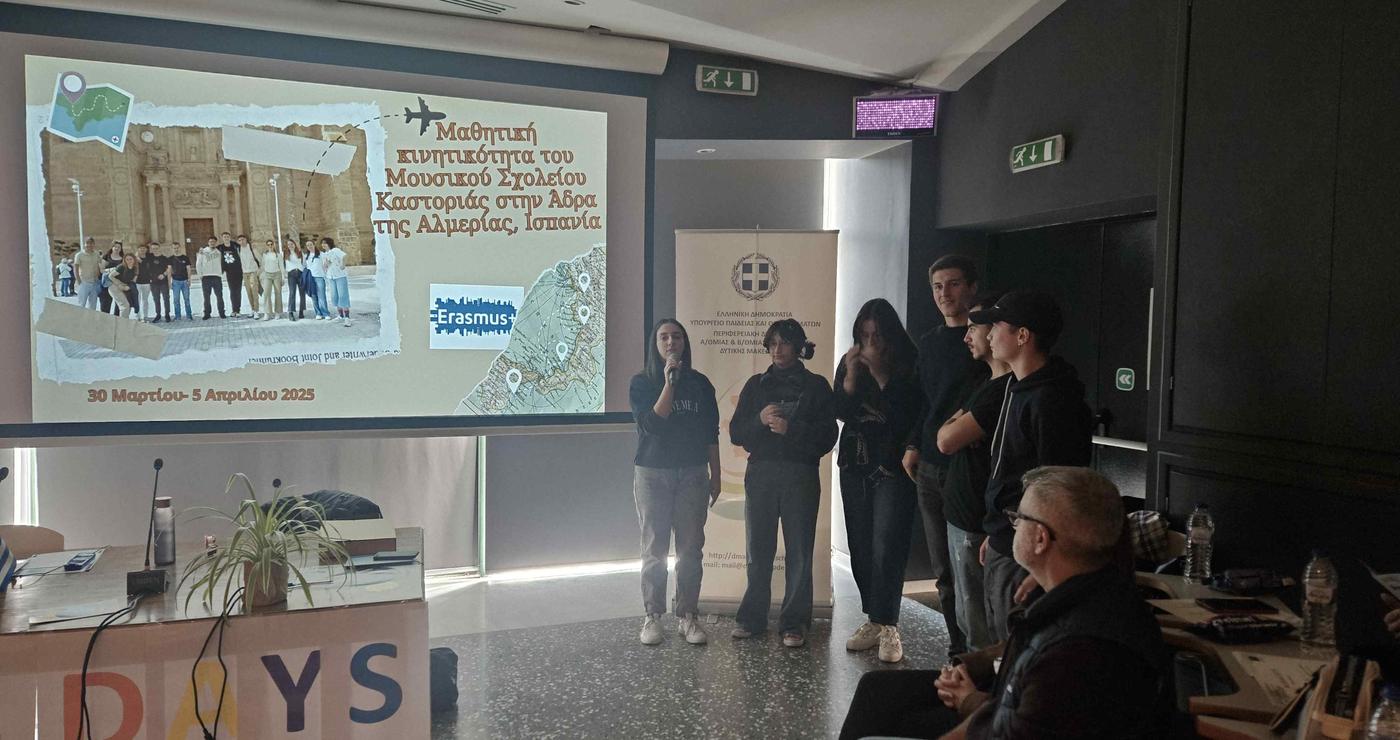 A group of people stand in a room during the Erasmus Days 2025 event, with a projected image of a historical scene and the Erasmus+ logo visible on a screen.