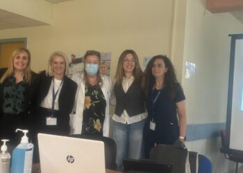 Μια ομάδα επαγγελματιών υγείας στέκεται χαμογελαστοί μπροστά από έναν φορητό υπολογιστή σε μια ημερίδα για τον αντιγριπικό εμβολιασμό στο Γενικό Νοσοκομείο Κοζάνης.