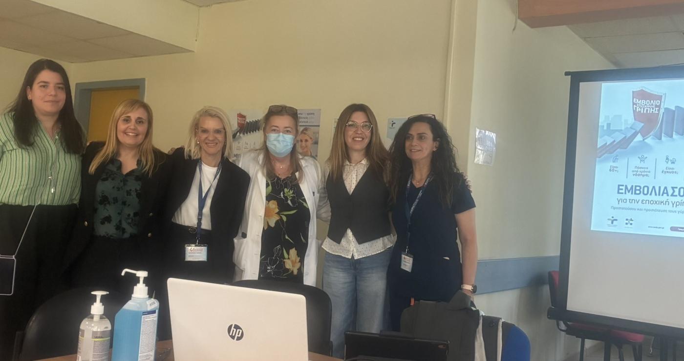 Μια ομάδα επαγγελματιών υγείας στέκεται χαμογελαστοί μπροστά από έναν φορητό υπολογιστή σε μια ημερίδα για τον αντιγριπικό εμβολιασμό στο Γενικό Νοσοκομείο Κοζάνης.