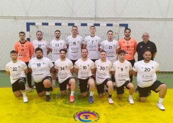 The handball team Αμύντας Αμυνταίου poses for a group photo on the court after a match, wearing dark and light uniforms.