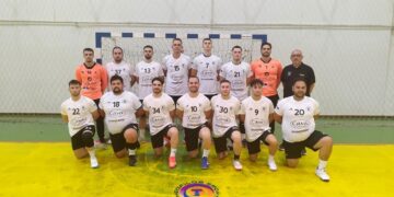 The handball team Αμύντας Αμυνταίου poses for a group photo on the court after a match, wearing dark and light uniforms.