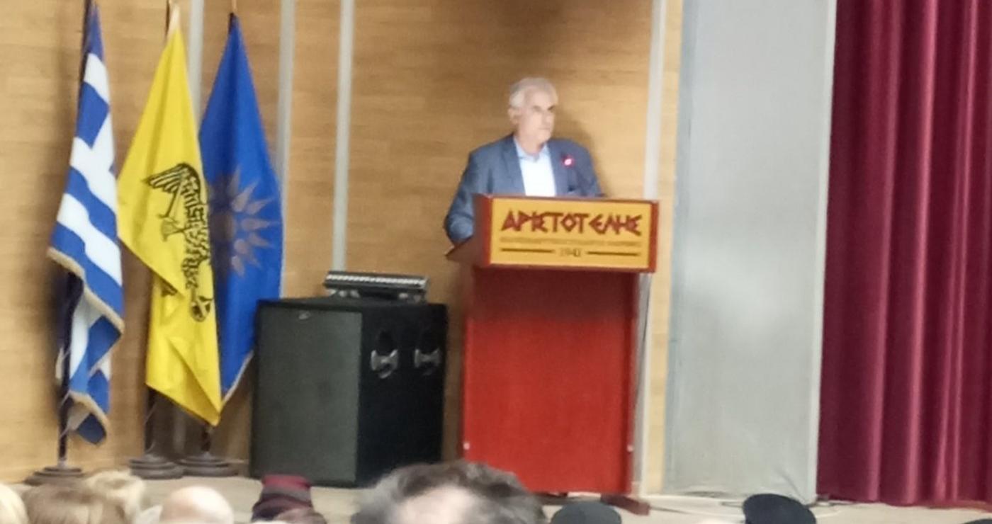 Ένας άνδρας μιλάει σε ένα κοινό στην παράσταση του θεατρικού εργαστηρίου Φλώρινας, με την ελληνική και την σημαία της Μητροπόλεως Φλωρίνης να δεσπόζουν στο βάθος.