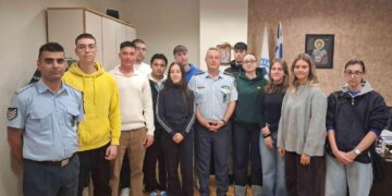 Μια ομάδα δόκιμων αστυφυλάκων στέκεται χαμογελαστοί σε έναν εσωτερικό χώρο, φορώντας καθημερινά ρούχα και στολές, με ελληνική σημαία στο βάθος, κατά την κατάταξή τους στη Δυτική Μακεδονία.