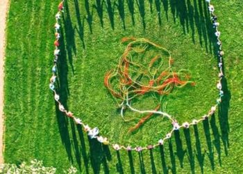 Άνθρωποι, συμπεριλαμβανομένων παιδιών και ατόμων με αναπηρία, σχηματίζουν έναν μεγάλο κύκλο σε ένα πράσινο λιβάδι στην Πτολεμαΐδα, συμμετέχοντας στο πολιτιστικό πρόγραμμα «Νήματα».