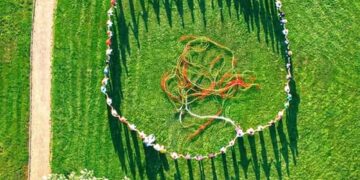 Άνθρωποι, συμπεριλαμβανομένων παιδιών και ατόμων με αναπηρία, σχηματίζουν έναν μεγάλο κύκλο σε ένα πράσινο λιβάδι στην Πτολεμαΐδα, συμμετέχοντας στο πολιτιστικό πρόγραμμα «Νήματα».