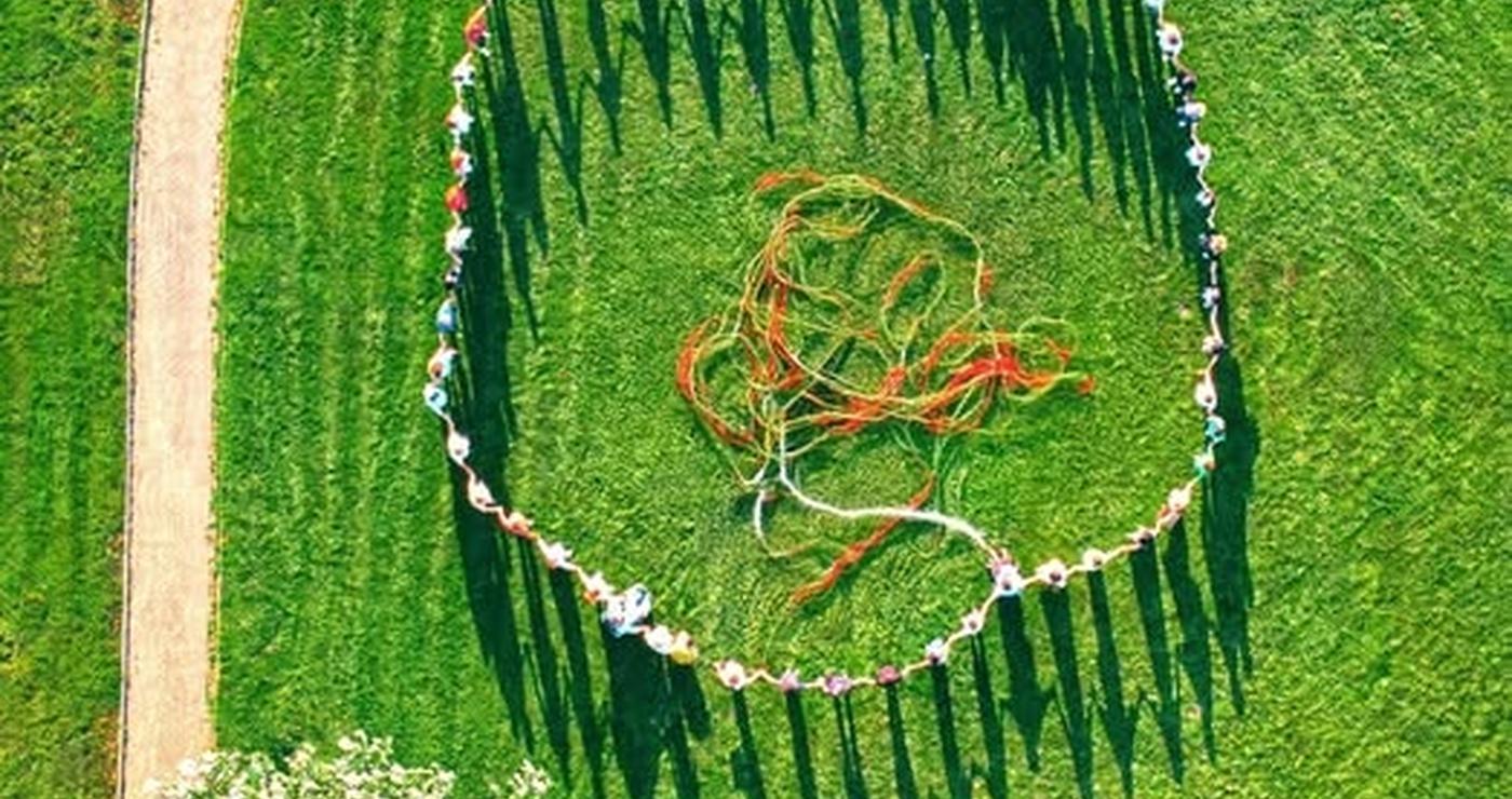 Άνθρωποι, συμπεριλαμβανομένων παιδιών και ατόμων με αναπηρία, σχηματίζουν έναν μεγάλο κύκλο σε ένα πράσινο λιβάδι στην Πτολεμαΐδα, συμμετέχοντας στο πολιτιστικό πρόγραμμα «Νήματα».