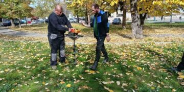 Δύο άνδρες συζητούν δίπλα σε ένα δενδρύλλιο κατά τη διάρκεια των δενδροφυτεύσεων στη Φλώρινα, με φθινοπωρινό τοπίο στο βάθος.