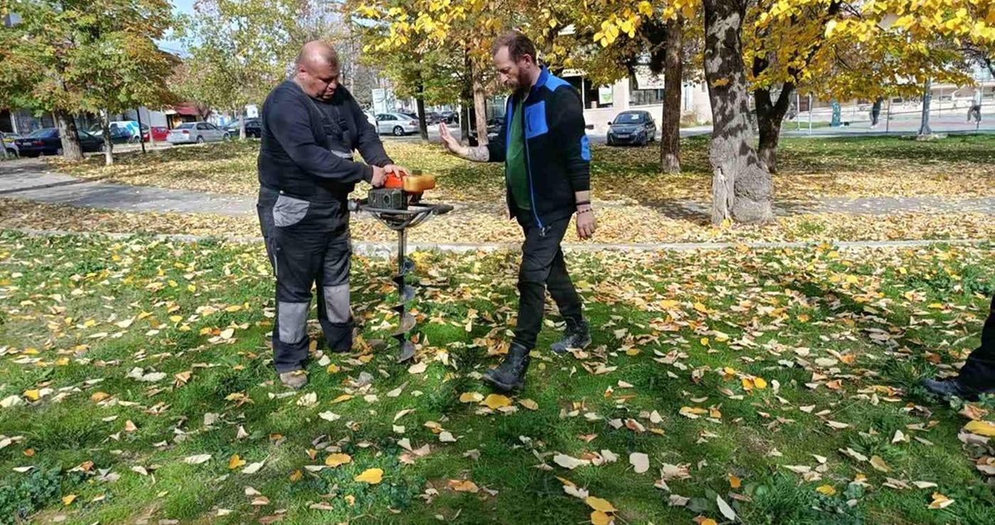 Δύο άνδρες συζητούν δίπλα σε ένα δενδρύλλιο κατά τη διάρκεια των δενδροφυτεύσεων στη Φλώρινα, με φθινοπωρινό τοπίο στο βάθος.
