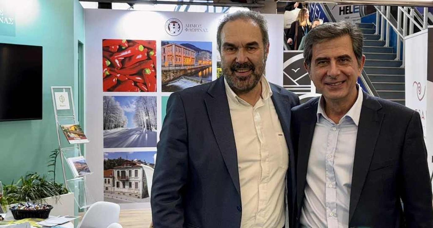 Δύο άνδρες χαμογελούν στο περίπτερο του Δήμου Φλώρινας στην Philoxenia 2025, προβάλλοντας την Φλώρινα ως προορισμό.
