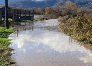 A flooded rural road in Florina, with mountains visible in the background, showcasing the extent of the Πλημμύρες Φλώρινας.