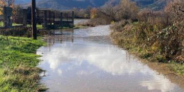 A flooded rural road in Florina, with mountains visible in the background, showcasing the extent of the Πλημμύρες Φλώρινας.