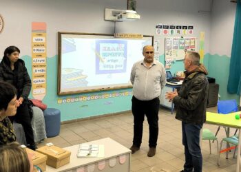 Μια δασκάλα, ένας άνδρας και μια ομάδα μαθητών συζητούν στο νέο Τμήμα Ένταξης Αμυνταίου, με τον άνδρα να παρουσιάζει κάτι με ενθουσιασμό.