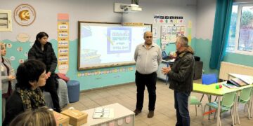 Μια δασκάλα, ένας άνδρας και μια ομάδα μαθητών συζητούν στο νέο Τμήμα Ένταξης Αμυνταίου, με τον άνδρα να παρουσιάζει κάτι με ενθουσιασμό.