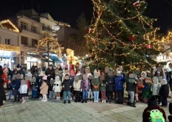 Πλήθος παιδιών και γονέων συγκεντρώνονται γύρω από ένα φωτισμένο χριστουγεννιάτικο δέντρο στην Γιορτή Ζαχαρωτών στη Φλώρινα.
