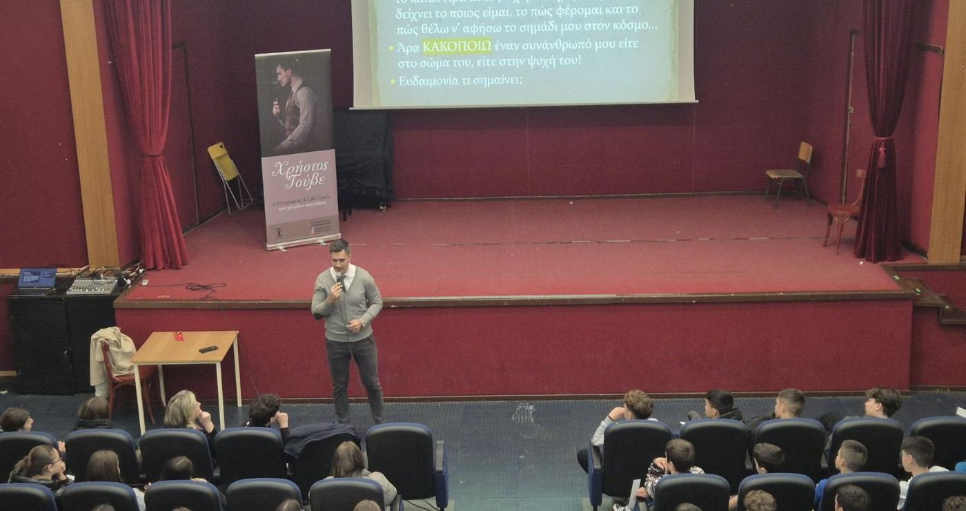 Ο συγγραφέας και Life Coach Χρήστος Τούβε μιλάει στους μαθητές του Γυμνασίου Αμυνταίου για τον σχολικό εκφοβισμό, ενώ μια διαφάνεια προβάλλεται στο φόντο.