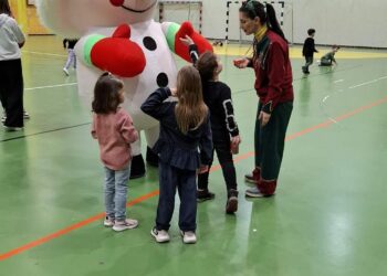 Μια μεγάλη χριστουγεννιάτικη μασκότ στέκεται ανάμεσα σε μια ομάδα παιδιών στο ΔΑΚ Αμυνταίου, κατά τη διάρκεια της χριστουγεννιάτικης εκδήλωσης.