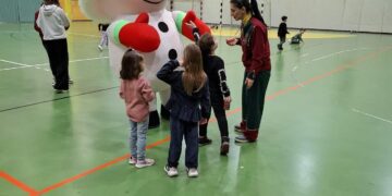 Μια μεγάλη χριστουγεννιάτικη μασκότ στέκεται ανάμεσα σε μια ομάδα παιδιών στο ΔΑΚ Αμυνταίου, κατά τη διάρκεια της χριστουγεννιάτικης εκδήλωσης.