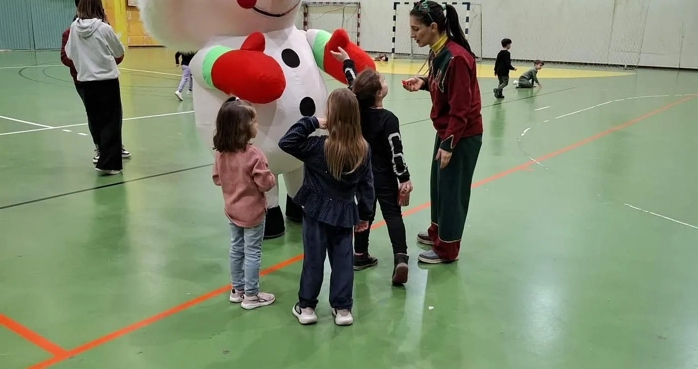 Μια μεγάλη χριστουγεννιάτικη μασκότ στέκεται ανάμεσα σε μια ομάδα παιδιών στο ΔΑΚ Αμυνταίου, κατά τη διάρκεια της χριστουγεννιάτικης εκδήλωσης.
