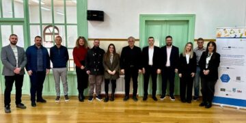 Ομάδα ανθρώπων στέκεται μπροστά από μια σειρά από πράσινες πόρτες στο Τραμπάντζειο Γυμνάσιο στη Σιάτιστα, κατά την εναρκτήρια συνάντηση του έργου Δήμος Βοΐου ReWaste.