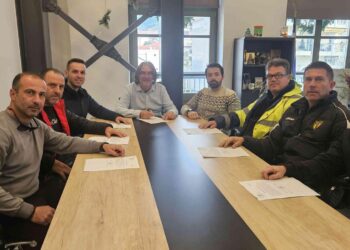 Νέοι εργαζόμενοι του δήμου Σερβίων κάθονται γύρω από ένα μεγάλο τραπέζι υπογράφοντας συμβάσεις εργασίας.