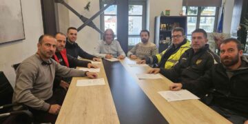 Νέοι εργαζόμενοι του δήμου Σερβίων κάθονται γύρω από ένα μεγάλο τραπέζι υπογράφοντας συμβάσεις εργασίας.