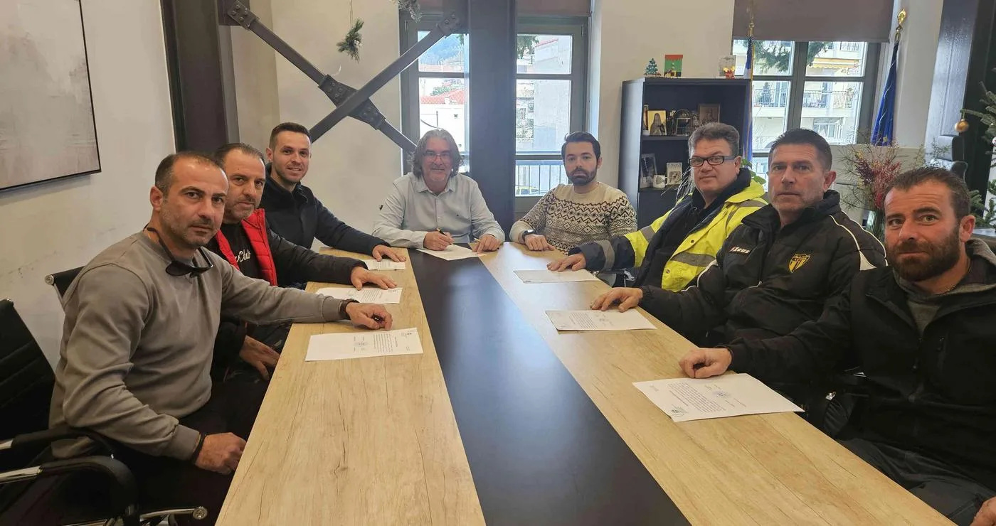 Νέοι εργαζόμενοι του δήμου Σερβίων κάθονται γύρω από ένα μεγάλο τραπέζι υπογράφοντας συμβάσεις εργασίας.