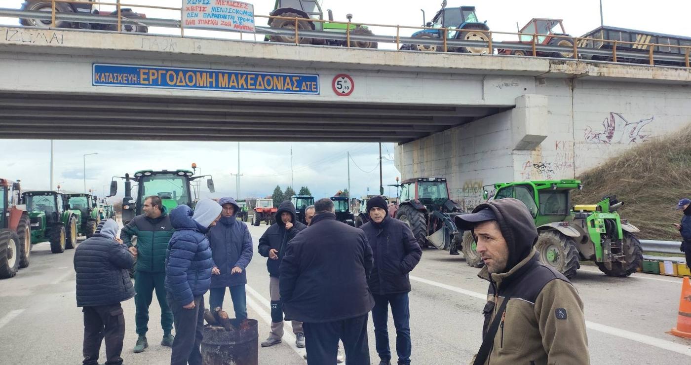 Αγρότες στέκονται κοντά στα τρακτέρ τους στον κόμβο Φιλώτα, ενώ κλείνουν τον δρόμο κατά τη διάρκεια του μπλόκο Φιλώτα.