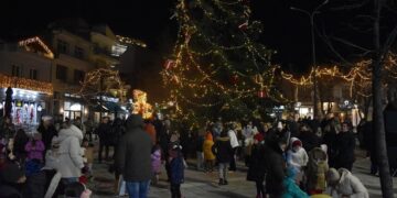 Ένα πλήθος ανθρώπων συγκεντρώνεται γύρω από το φωτισμένο χριστουγεννιάτικο δέντρο στην πλατεία της Φλώρινας κατά τη διάρκεια των χριστουγεννιάτικων εκδηλώσεων.