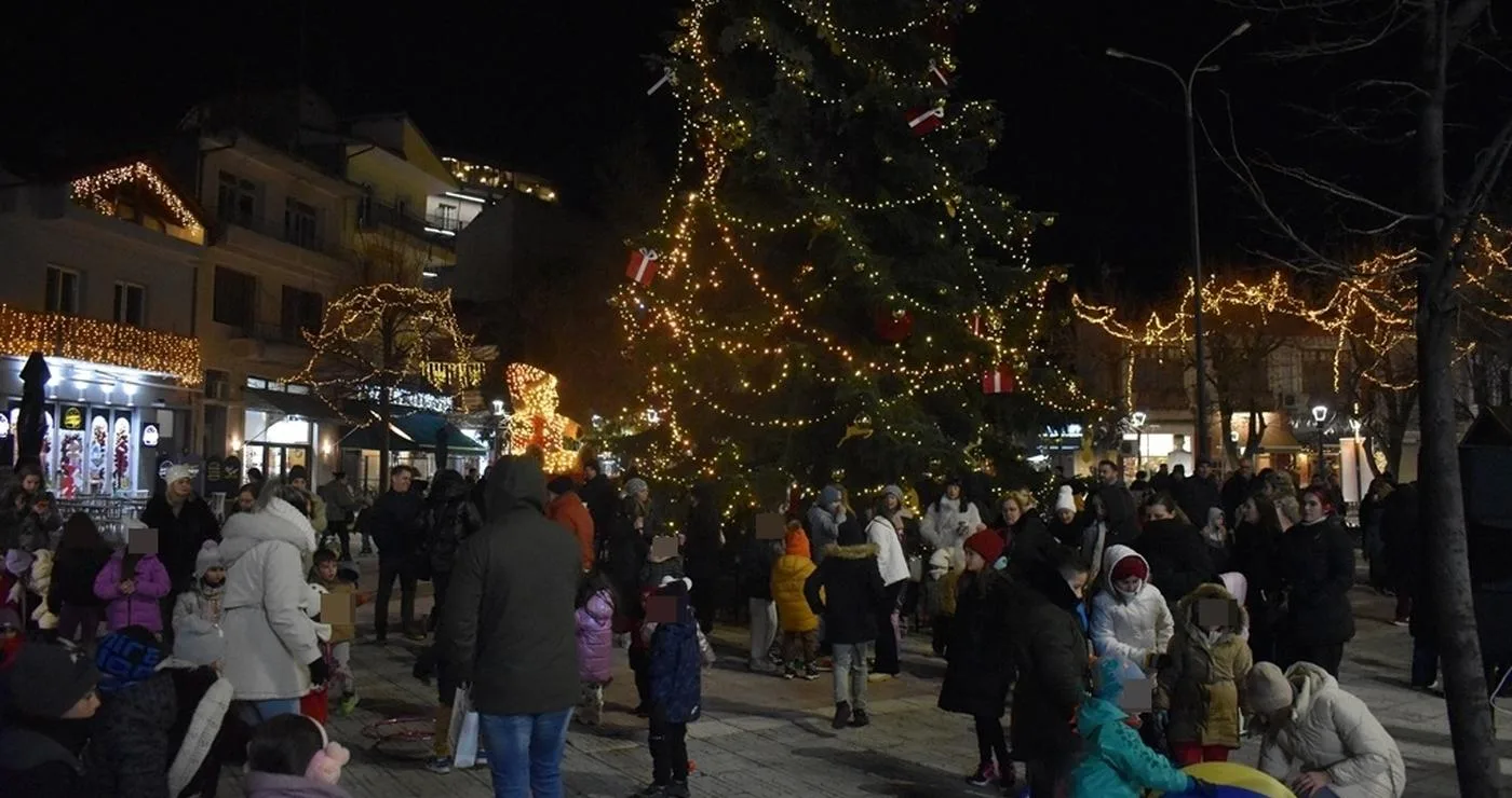 Ένα πλήθος ανθρώπων συγκεντρώνεται γύρω από το φωτισμένο χριστουγεννιάτικο δέντρο στην πλατεία της Φλώρινας κατά τη διάρκεια των χριστουγεννιάτικων εκδηλώσεων.
