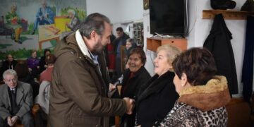 Ο δήμαρχος Φλώρινας ανταλλάσσει χειραψία με μια ηλικιωμένη γυναίκα κατά τη διάρκεια των Χριστουγεννιάτικων επισκέψεων σε ένα ΚΑΠΗ.