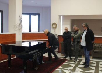 Άνδρες παρακολουθούν έναν άνδρα να στήνει το νέο πιάνο στο Δημοτικό Ωδείο Σερβίων, μια σημαντική προσθήκη για τη μουσική εκπαίδευση.