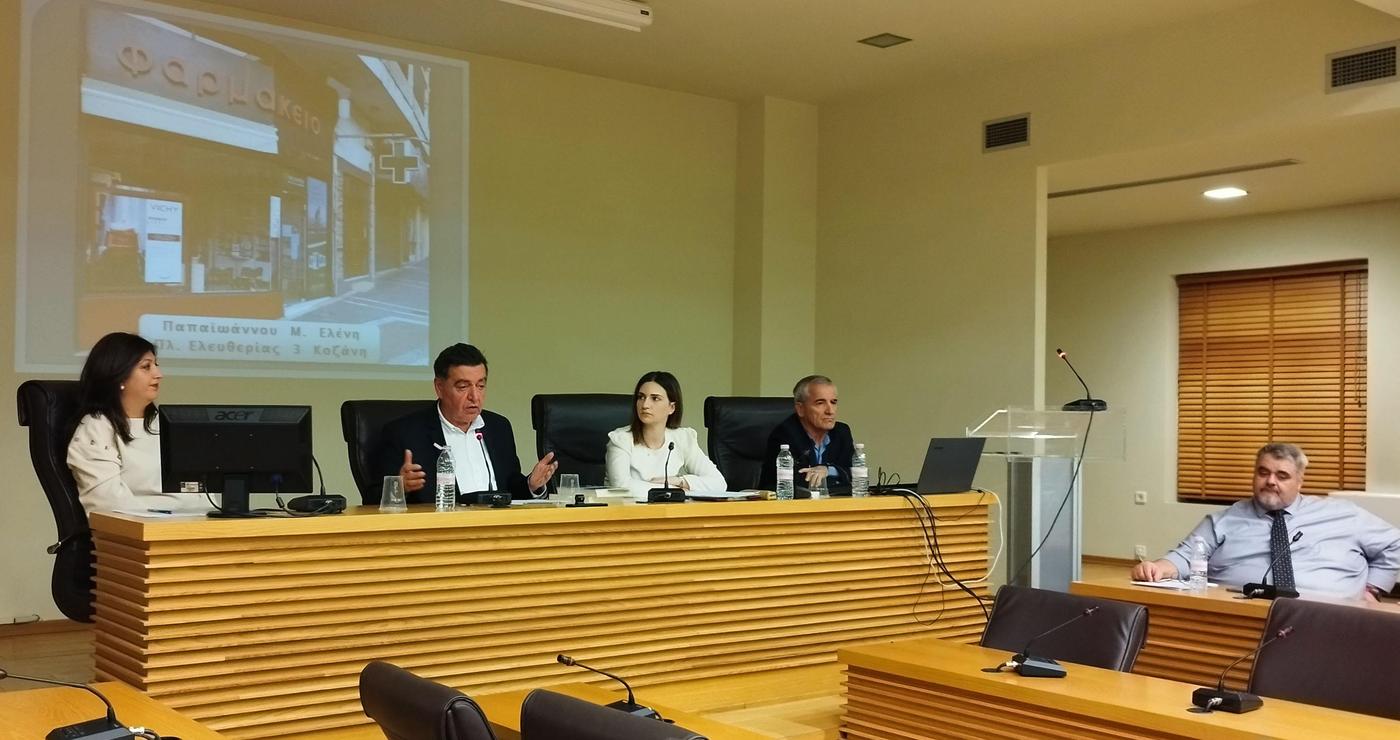 Μια ομάδα ανθρώπων κάθεται γύρω από ένα μεγάλο τραπέζι σε ένα σύγχρονο συνεδριακό δωμάτιο, παρουσιάζοντας την Εβδομάδα Εράτυρας σε μια ημερίδα στο Κοβεντάρειο.