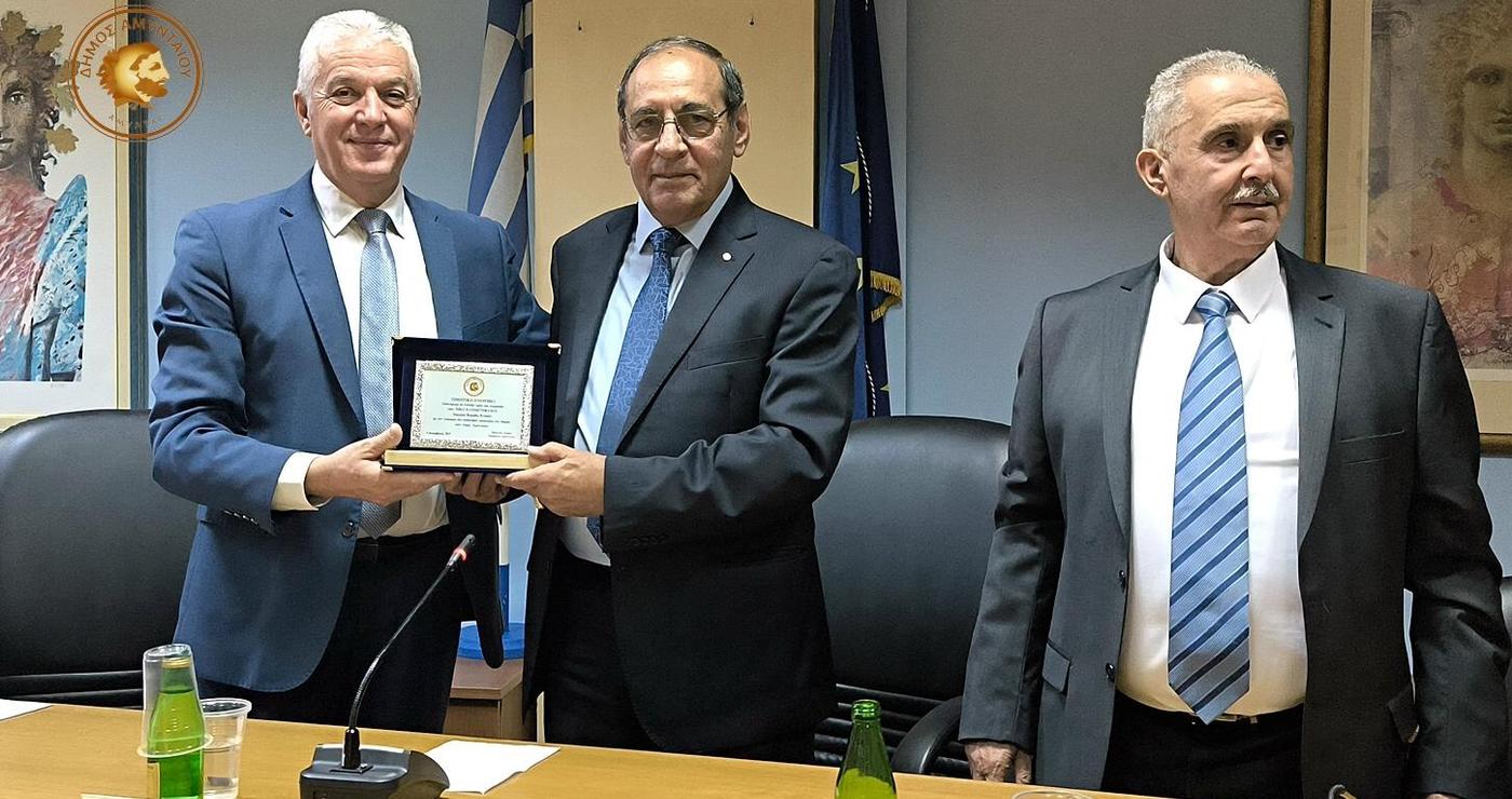 Τρεις άνδρες ανταλλάσσουν ένα έγγραφο αδελφοποίησης Αμυνταίου – Καραβά σε επίσημη τελετή, συμβολίζοντας τον ιστορικό δεσμό των δύο δήμων.