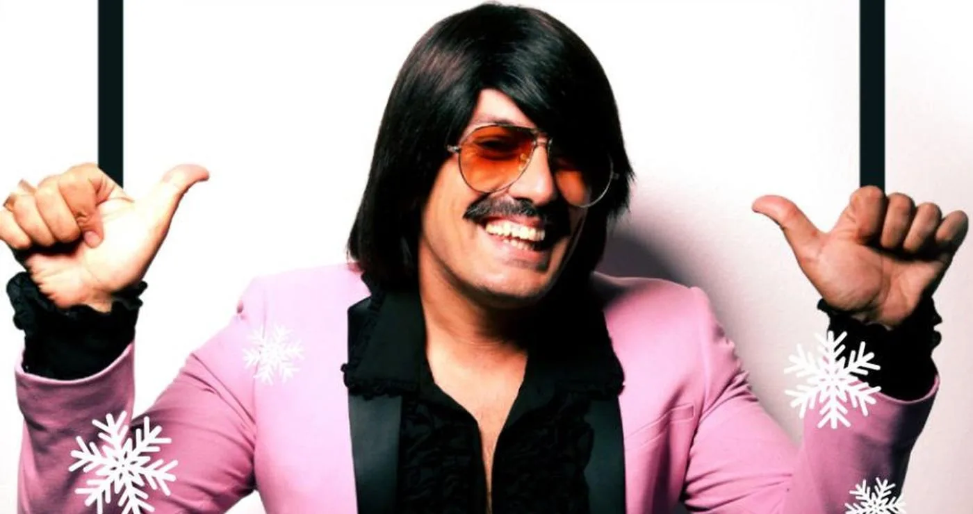 Ο Τόνι Σφήνος ποζάρει χαμογελαστός για την Καστοριά Πρωτοχρονιά, φορώντας ένα ροζ σακάκι και με χιονονιφάδες γύρω του.