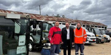 Τρία άτομα στέκονται δίπλα σε ένα ηλεκτροκίνητο όχημα σάρωσης με τον Δήμο Φλώρινας στο φόντο, παρουσιάζοντας τα νέα ηλεκτροκίνητα οχήματα Φλώρινα.