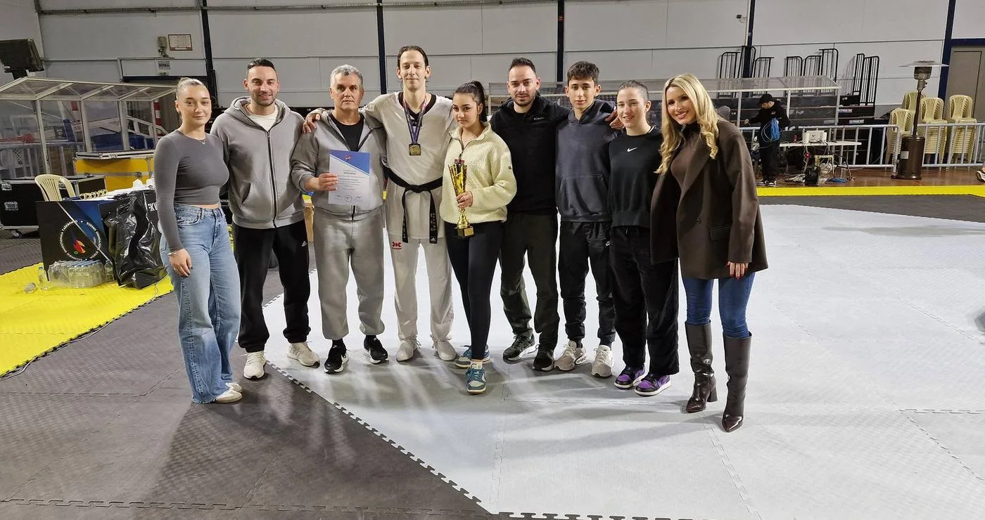 Ο Απόστολος Τεληκωστόγλου, αθλητής του Taekwondo, στέκεται με την ομάδα του Μακεδονικής Δύναμης Κοζάνης, χαμογελαστοί και περήφανοι μετά την κατάκτηση του χρυσού μεταλλίου στο Πανελλήνιο Πρωτάθλημα.