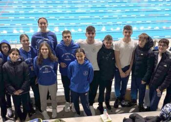 Η ομάδα κολύμβησης της Κοζάνης στέκεται περήφανα δίπλα στην πισίνα στην Καβάλα, φορώντας τα μπλε τους φλιτζάνια με το λογότυπο, μετά τους αγώνες κολύμβησης.