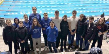 Η ομάδα κολύμβησης της Κοζάνης στέκεται περήφανα δίπλα στην πισίνα στην Καβάλα, φορώντας τα μπλε τους φλιτζάνια με το λογότυπο, μετά τους αγώνες κολύμβησης.