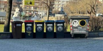 Στην Φλώρινα, μια σειρά από νέους, προσβάσιμους κάδους απορριμμάτων βρίσκονται τοποθετημένοι σε πλακόστρωτο δρόμο, δίπλα σε ένα πάρκο και με φόντο τα βουνά, ενισχύοντας την προσβασιμότητα στην πόλη.