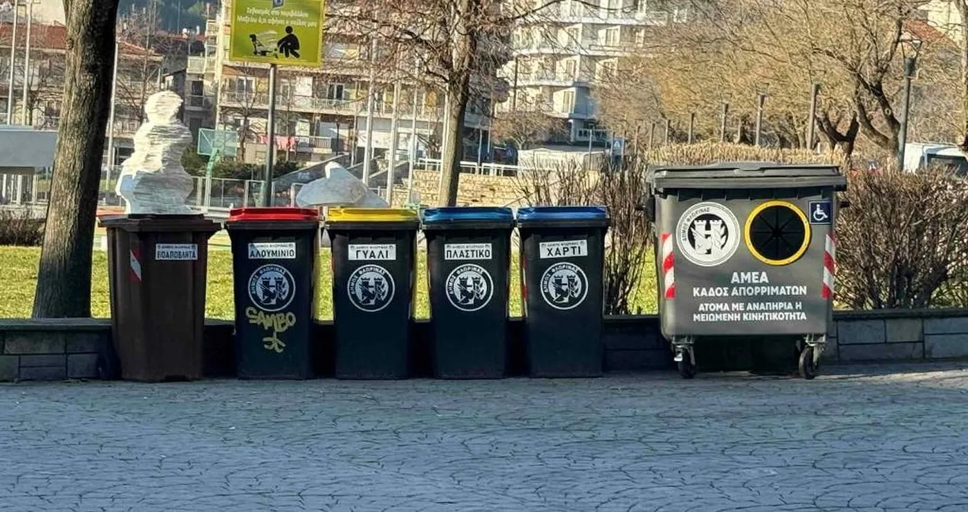 Στην Φλώρινα, μια σειρά από νέους, προσβάσιμους κάδους απορριμμάτων βρίσκονται τοποθετημένοι σε πλακόστρωτο δρόμο, δίπλα σε ένα πάρκο και με φόντο τα βουνά, ενισχύοντας την προσβασιμότητα στην πόλη.