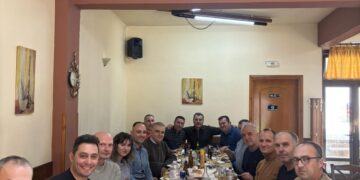 Αστυνομικοί του Αστυνομικού Τμήματος Βεύης Φλώρινας καθισμένοι γύρω από ένα τραπέζι γεμάτο με φαγητά κατά την κοπή πίτας.